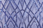a close-up view of a fabric with a repeating pattern of blue sequin designs. The pattern consists of various diamond shapes and lines, creating a visually striking and intricate design. The fabric appears to be a light purple color, which complements the blue sequin pattern. The image does not contain any text or additional objects, and the focus is solely on the detailed pattern of the sequin design.