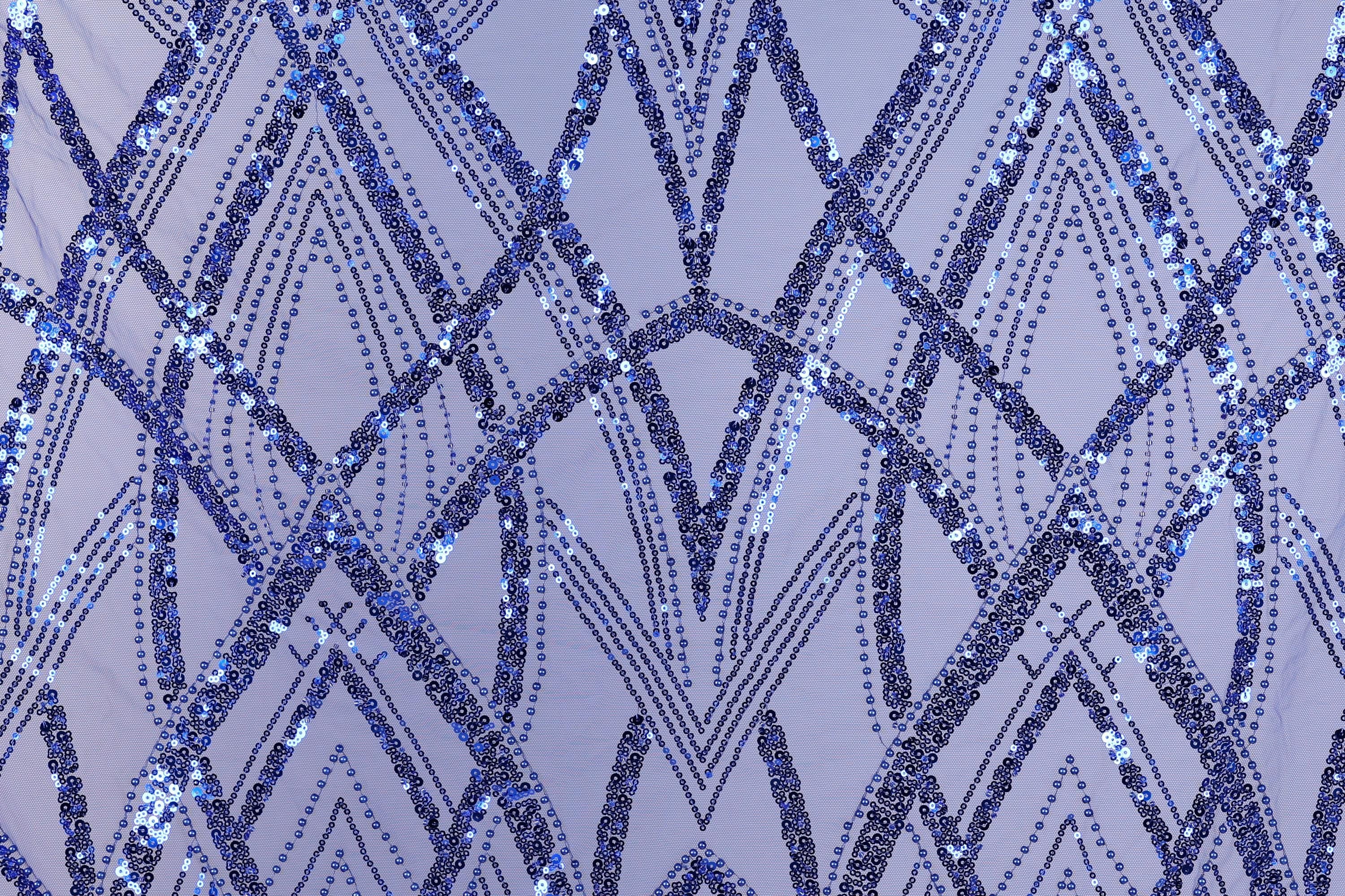 a close-up view of a fabric with a repeating pattern of blue sequin designs. The pattern consists of various diamond shapes and lines, creating a visually striking and intricate design. The fabric appears to be a light purple color, which complements the blue sequin pattern. The image does not contain any text or additional objects, and the focus is solely on the detailed pattern of the sequin design.