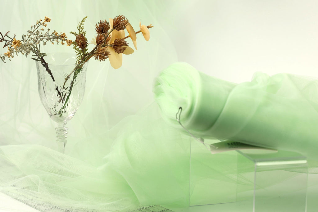 a glass vase with flowers and a green fabric draped over a table, creating a serene and elegant atmosphere.