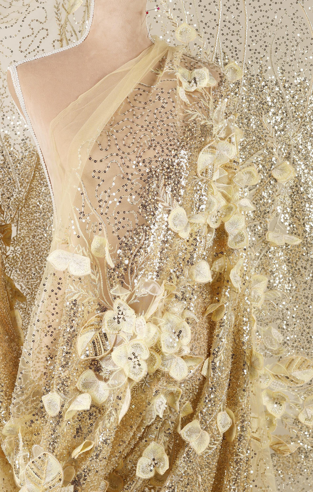The image is a close-up of a gold sequined dress with delicate white flowers.