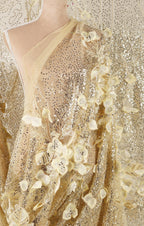 The image is a close-up of a gold sequined dress with delicate white flowers.
