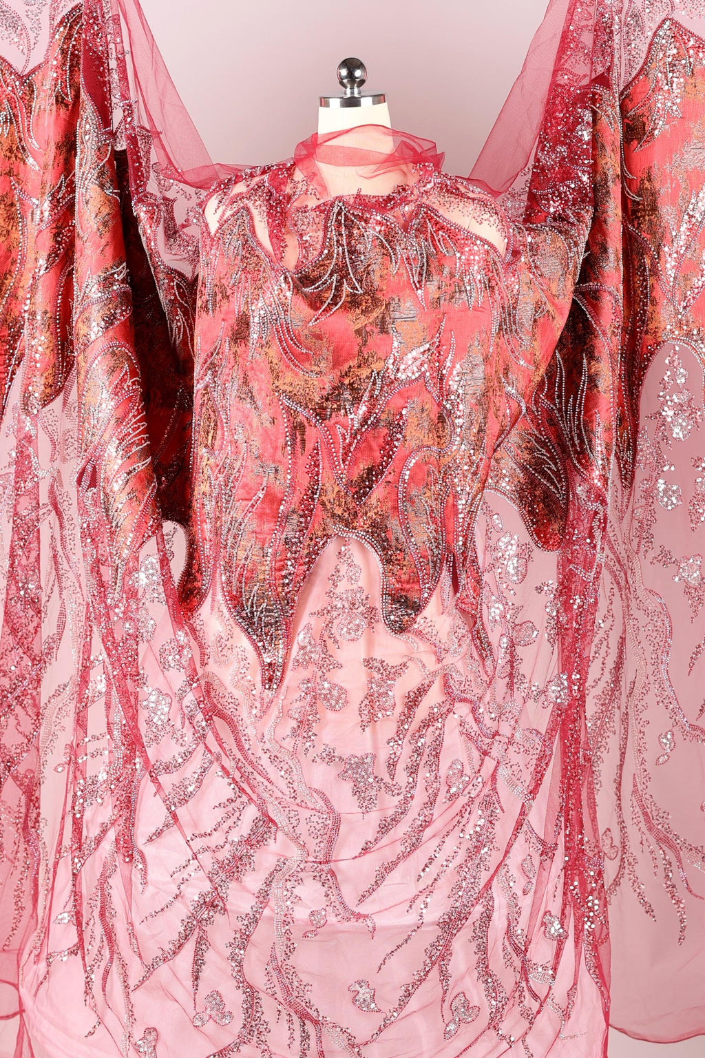 a pink and red fabric with a floral pattern, hanging on a mannequin.