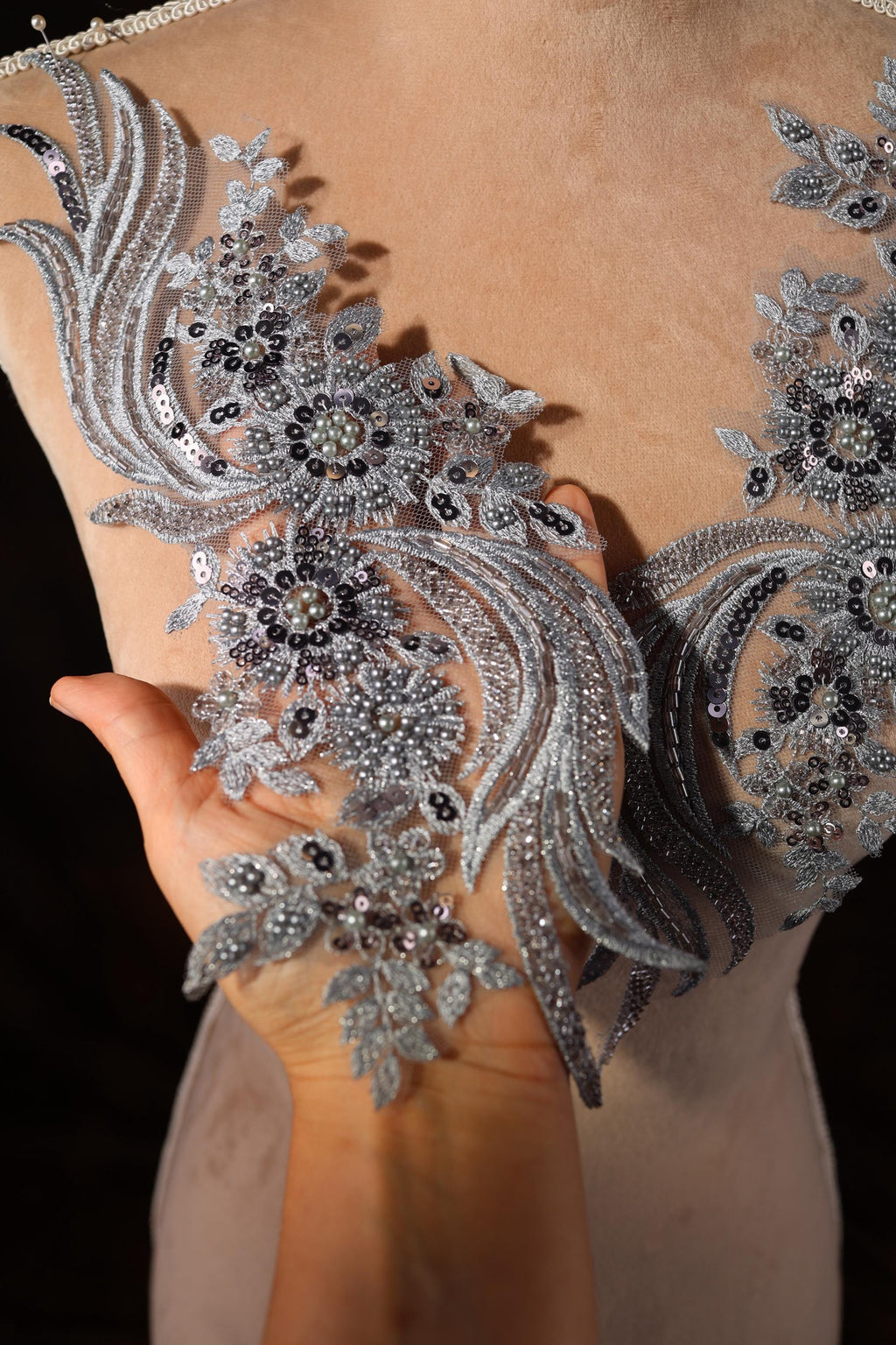 A close-up view of a person's hand holding a piece of fabric with intricate silver and black embroidered designs.