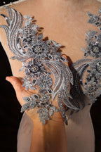 A close-up view of a person's hand holding a piece of fabric with intricate silver and black embroidered designs.