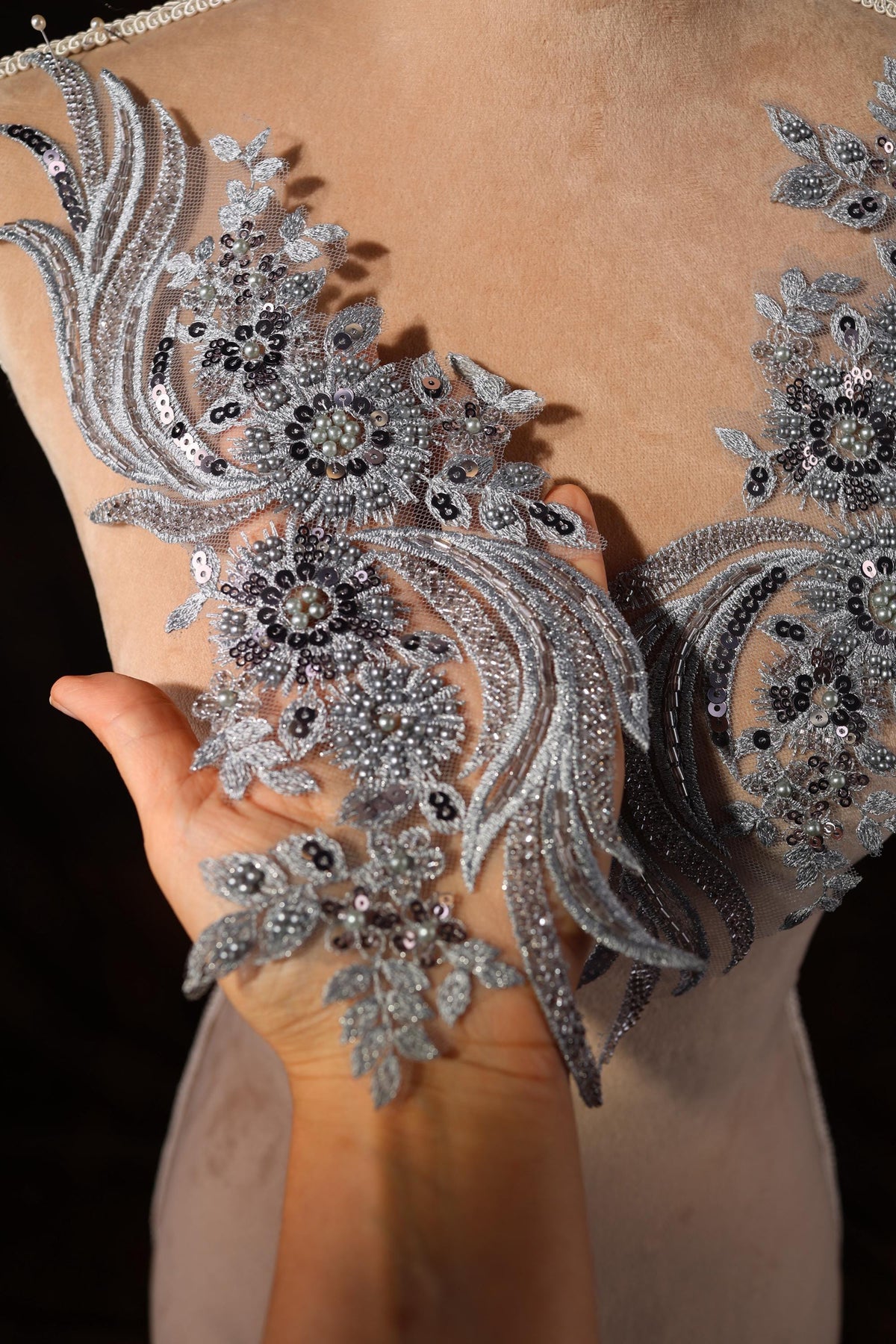 A close-up view of a person's hand holding a piece of fabric with intricate silver and black embroidered designs.