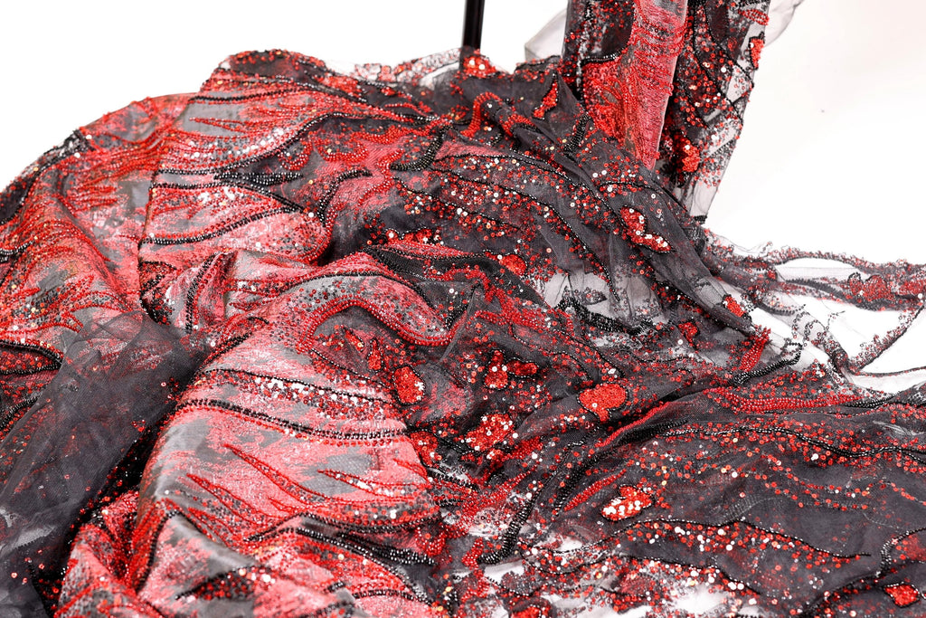 a close-up view of a fabric with a striking pattern of red and black sequins and beads. The fabric appears to be a sheer material, with a mix of black and red colors. The pattern is intricate and detailed, with the sequins and beads adding a touch of sparkle and glamour to the fabric.