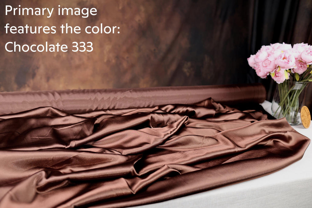 a close-up of a brown satin fabric, with a vase of pink flowers on a table next to it.