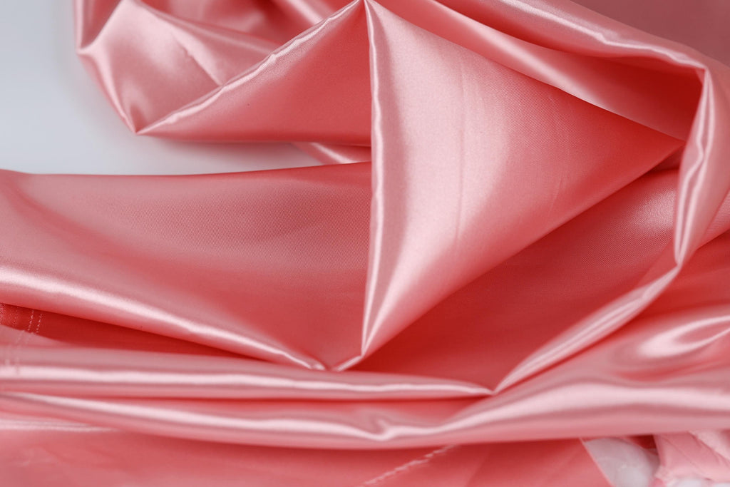 A close-up view of a soft, shiny pink satin fabric, with its folds and creases creating a textured and visually appealing surface.