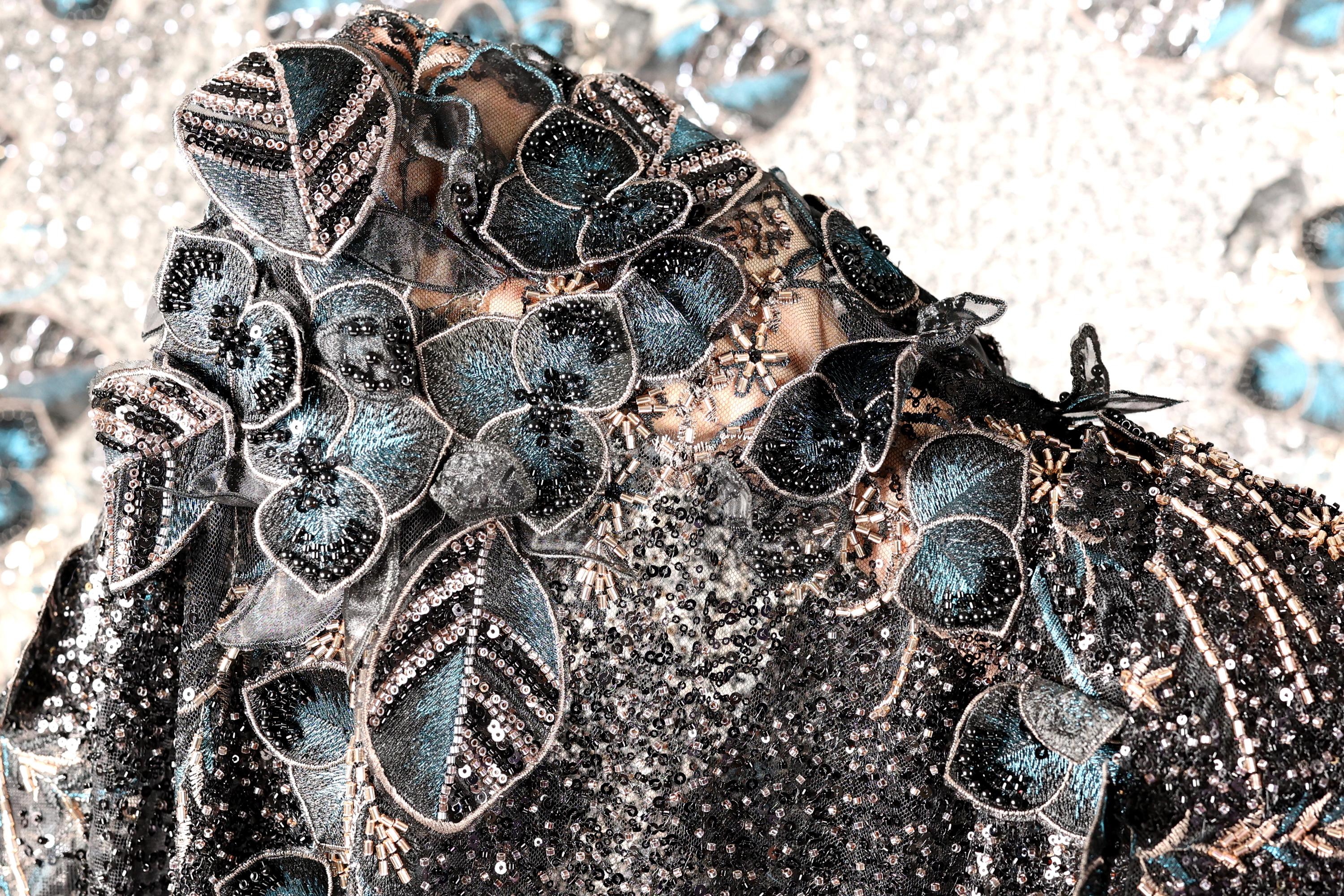 The image is a close-up of a black and blue sequined dress with intricate floral and leaf designs.
