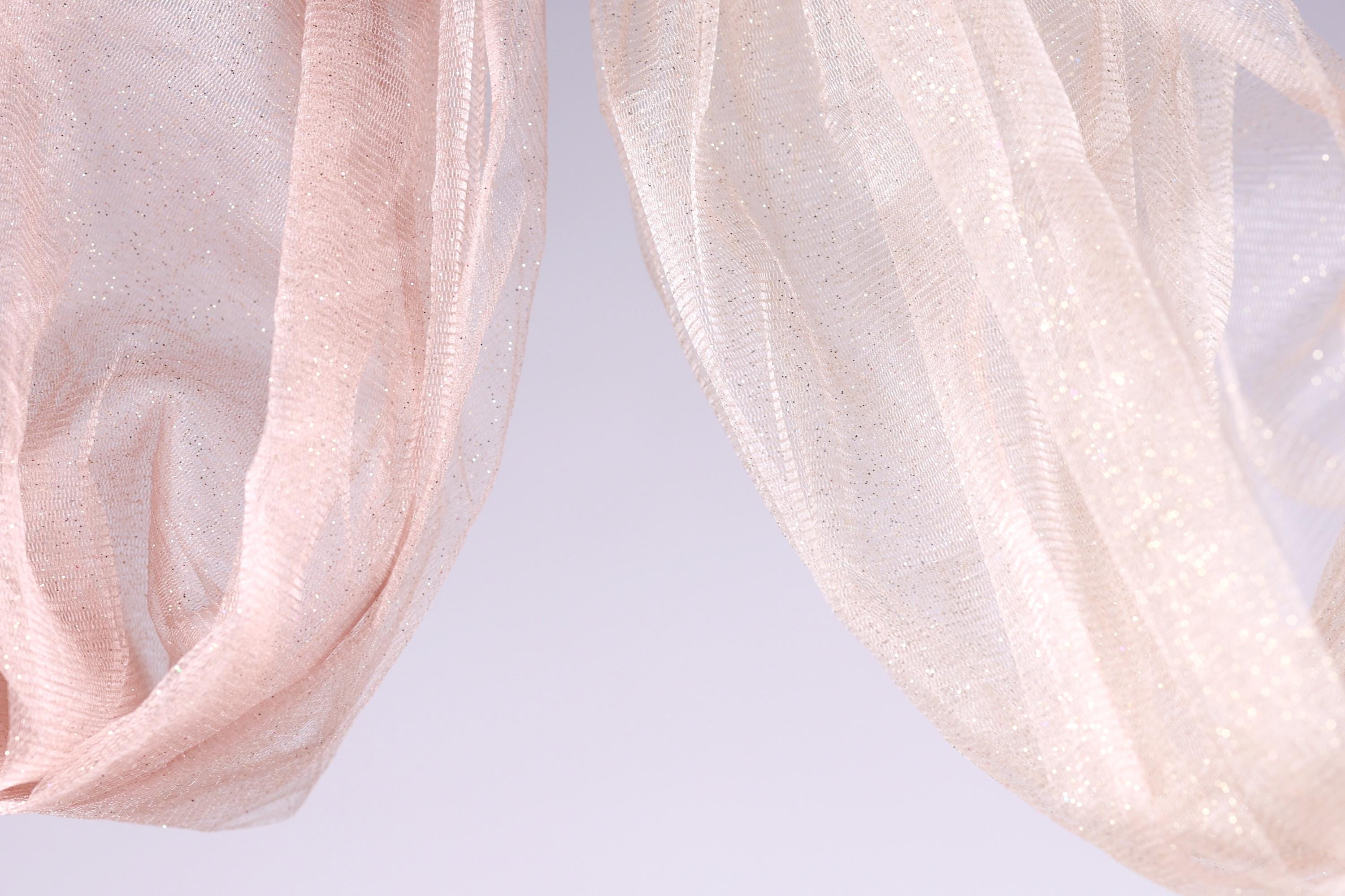 two light pink and white sheer fabric pieces hanging side by side against a light purple background.