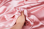 A hand with pink nail polish is holding a piece of pink satin fabric.