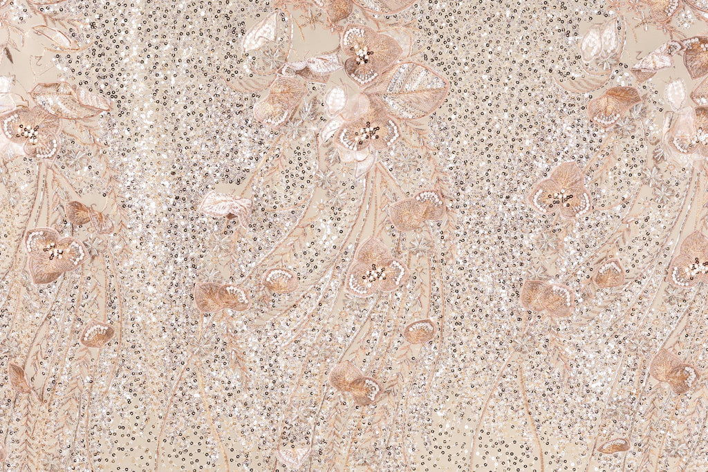 a close-up view of a fabric with a floral pattern, including various shades of pink and beige flowers and leaves. The fabric appears to be made of a shiny, glittery material, giving it a sparkling and elegant appearance.
