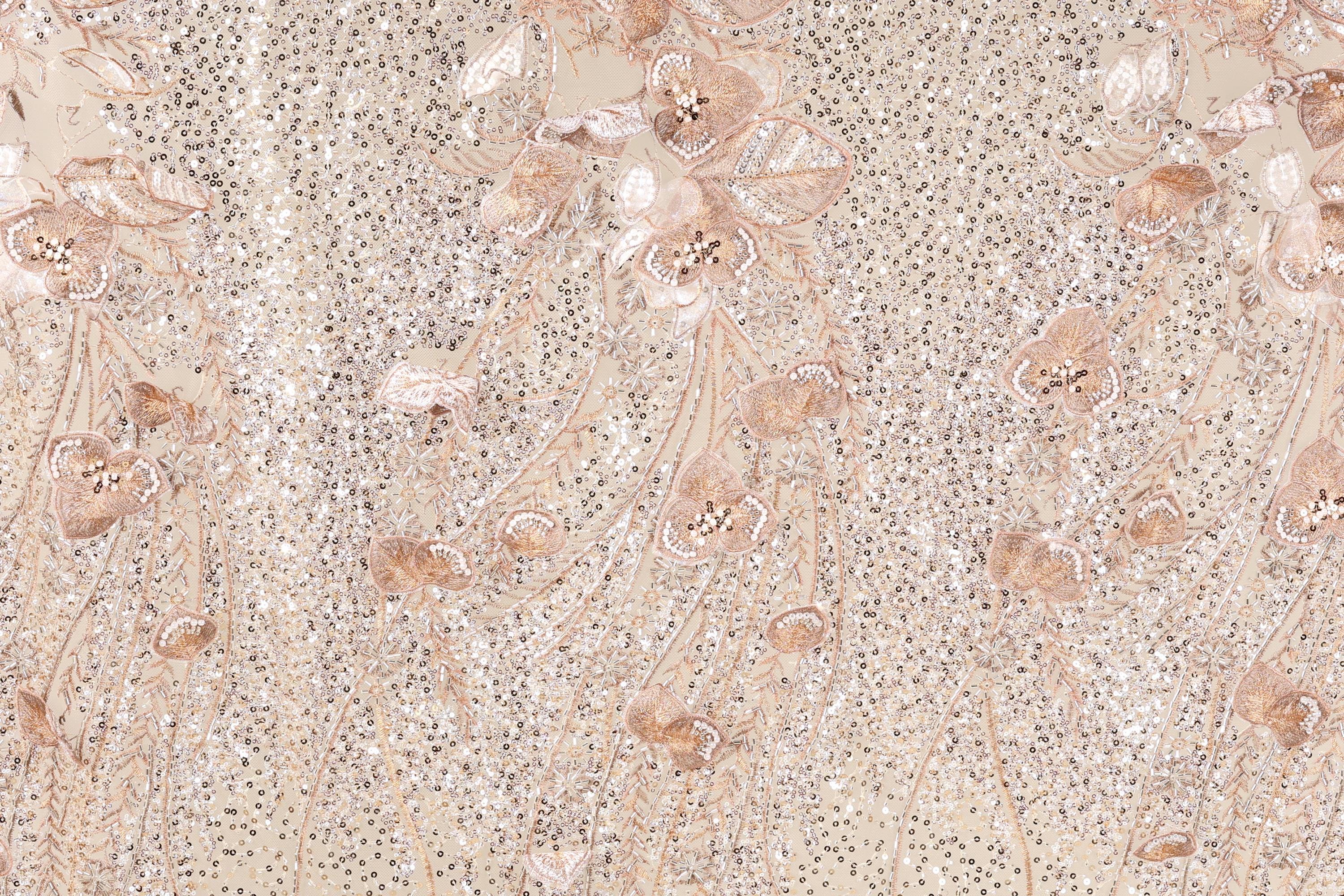 a close-up view of a fabric with a floral pattern, including various shades of pink and beige flowers and leaves. The fabric appears to be made of a shiny, glittery material, giving it a sparkling and elegant appearance.