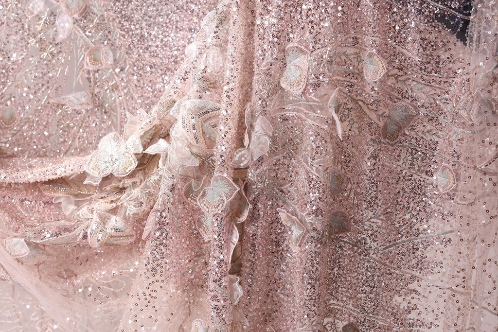 The image is a close-up of a delicate, pink, sequined fabric with intricate floral and leaf designs.