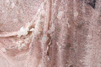 The image is a close-up of a delicate, pink, sequined fabric with intricate floral and leaf designs.