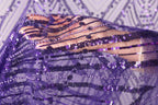 A close-up view of a hand holding a piece of sequin-covered fabric, with the fabric's pattern and sequin details visible.