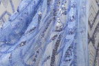 a close-up view of a delicate, sequined fabric with a blue and white color scheme. The fabric appears to be made of sheer material, with a pattern of small sequins and beads that create a visually striking and intricate design. The fabric is displayed in a close-up view, allowing for a detailed examination of its texture and appearance.