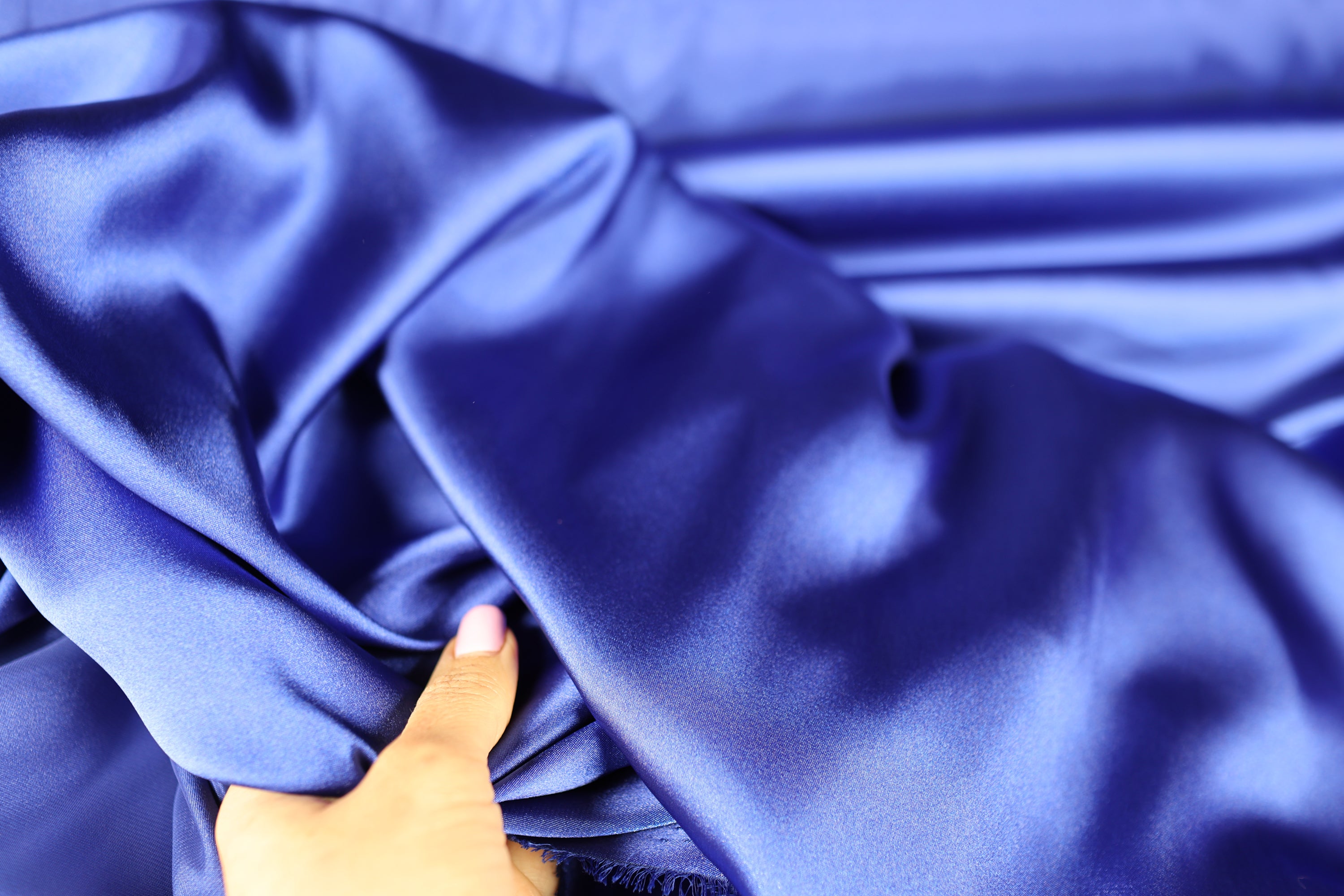 A hand is holding a piece of blue satin fabric, which appears to be a close-up view of the material.
