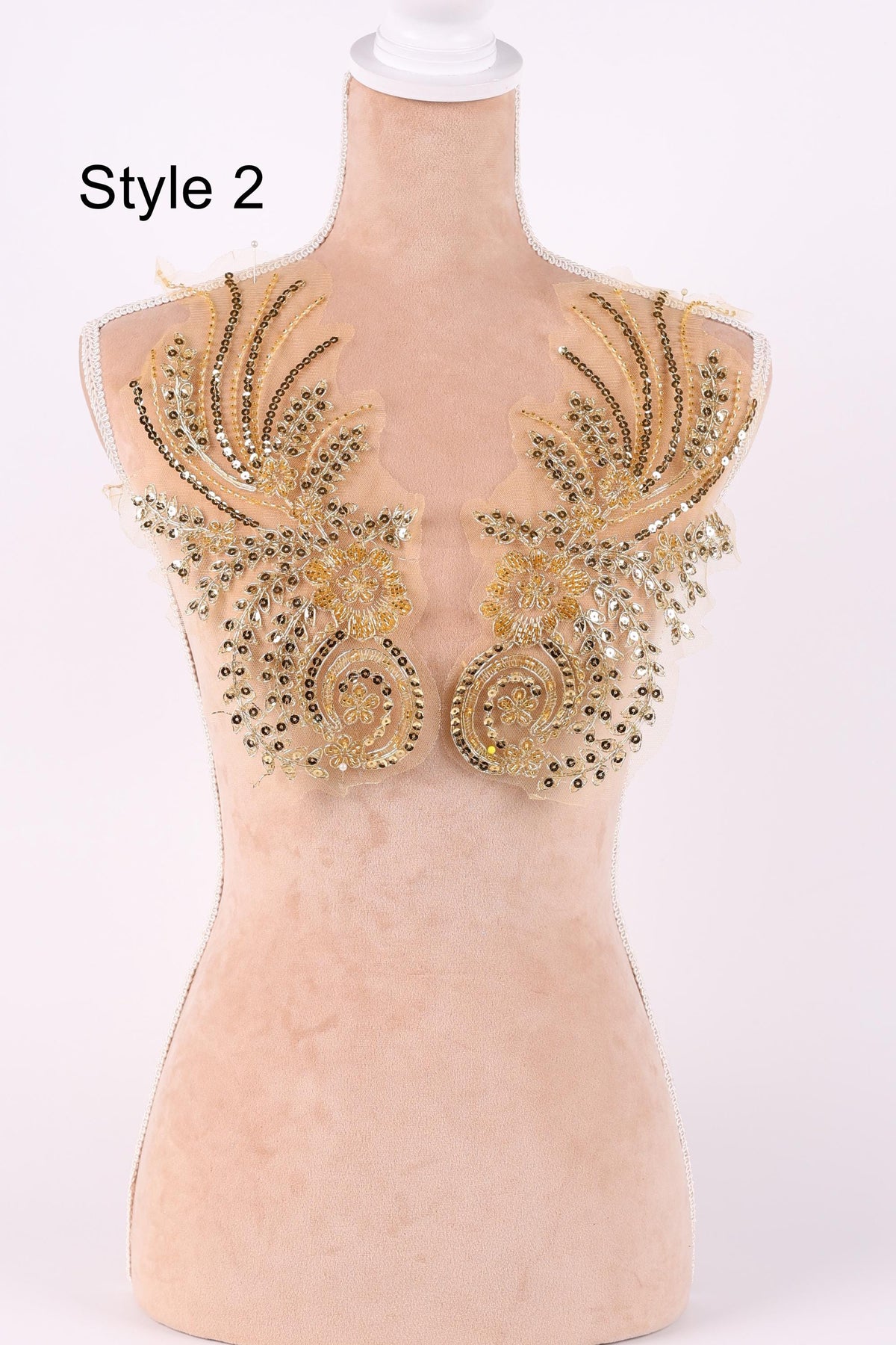 A mannequin with a beige body and gold embellishments on its shoulders, including a large, intricate design with a floral pattern.