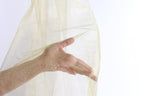A hand is holding a piece of gold-colored fabric or material, which appears to be a sheer or sheer-like material.