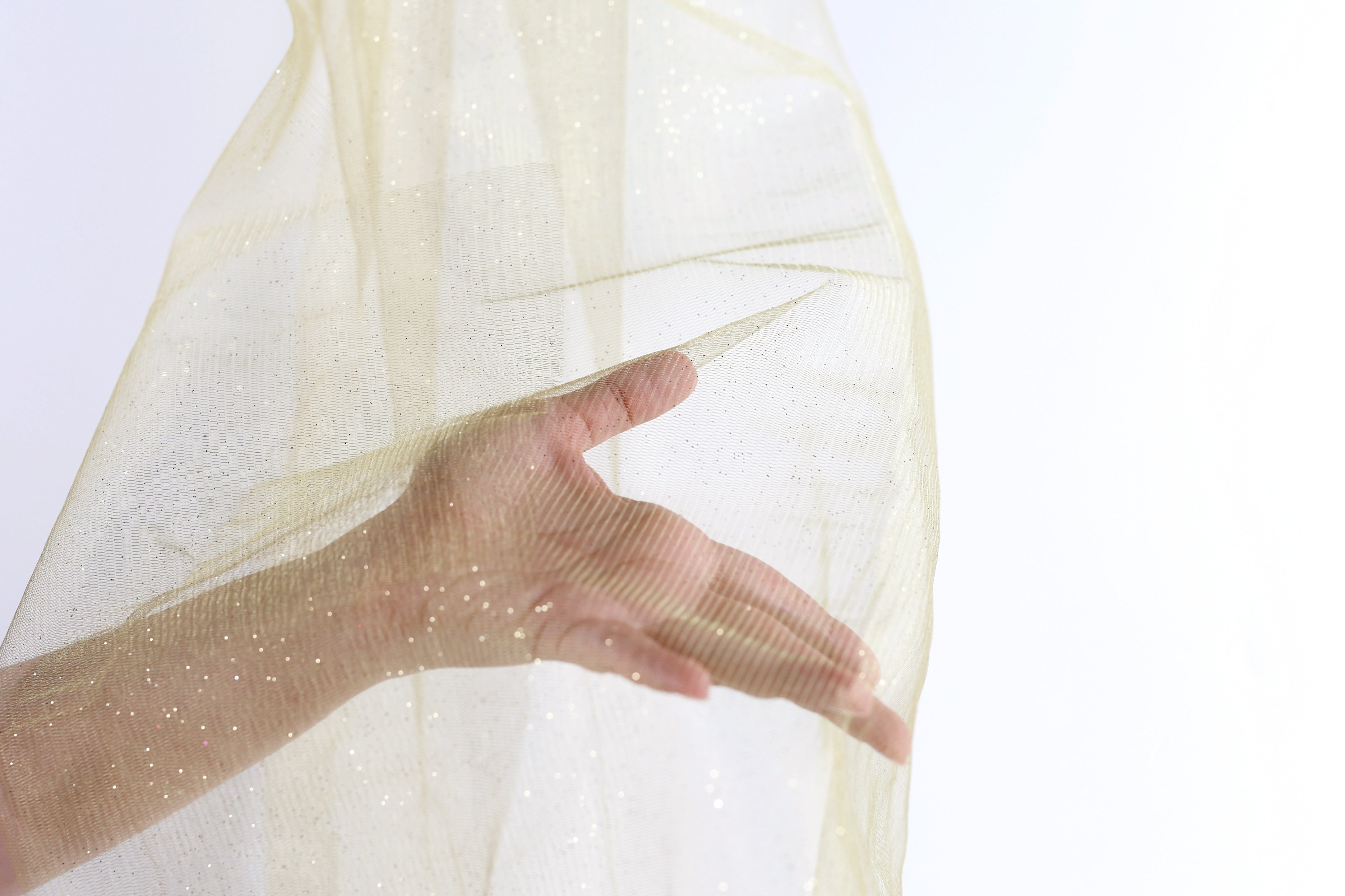 A hand is holding a piece of gold-colored fabric or material, which appears to be a sheer or sheer-like material.
