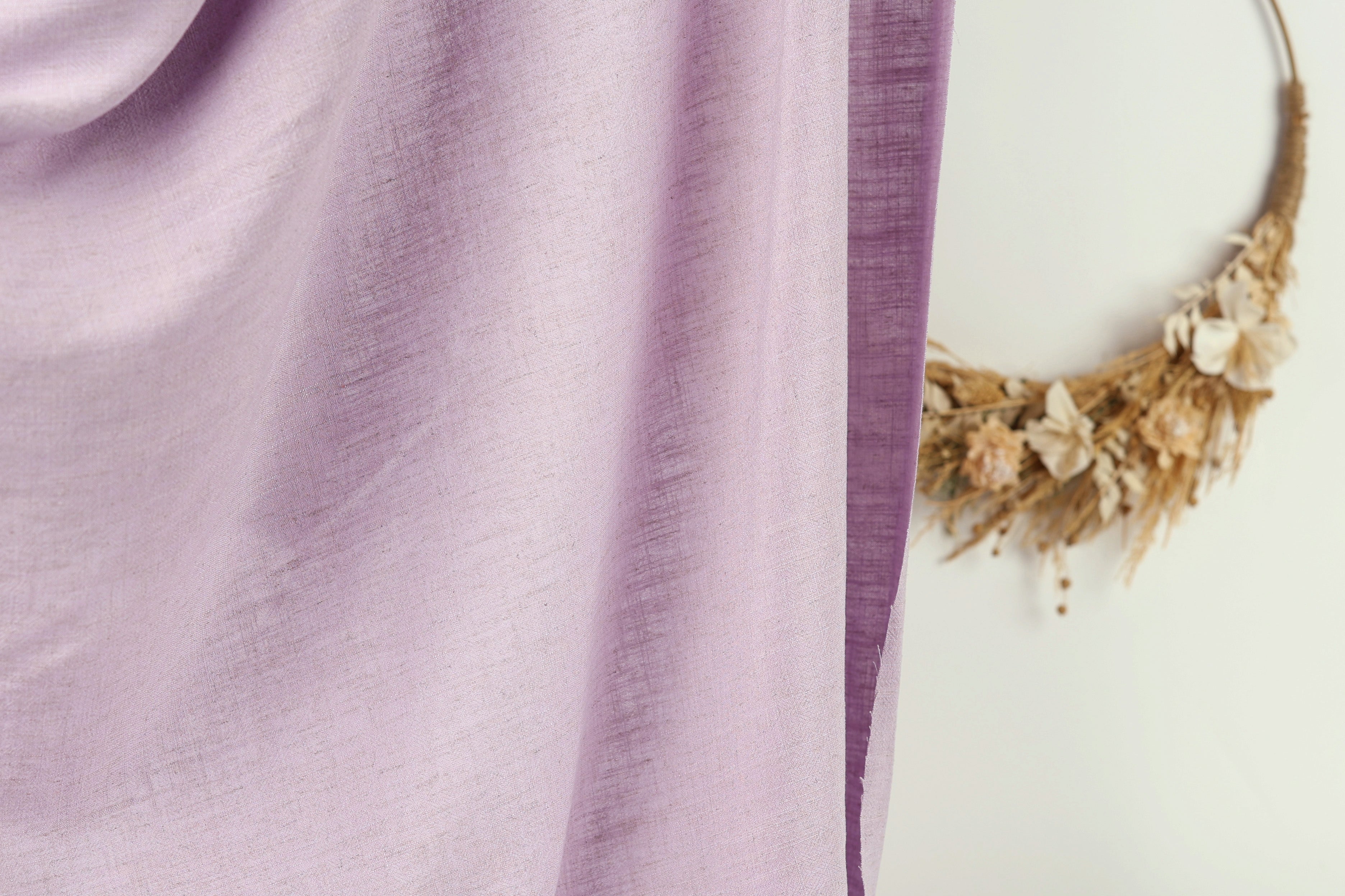 a close-up view of a purple fabric, with a wreath made of dried flowers hanging on a wall in the background.