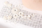 a close-up view of a delicate, white lace flower with sparkling crystal elements. The flower is placed on a transparent ruler, which is lying on a white surface. The ruler appears to be used for measuring or cutting the lace, possibly for a craft or sewing project.