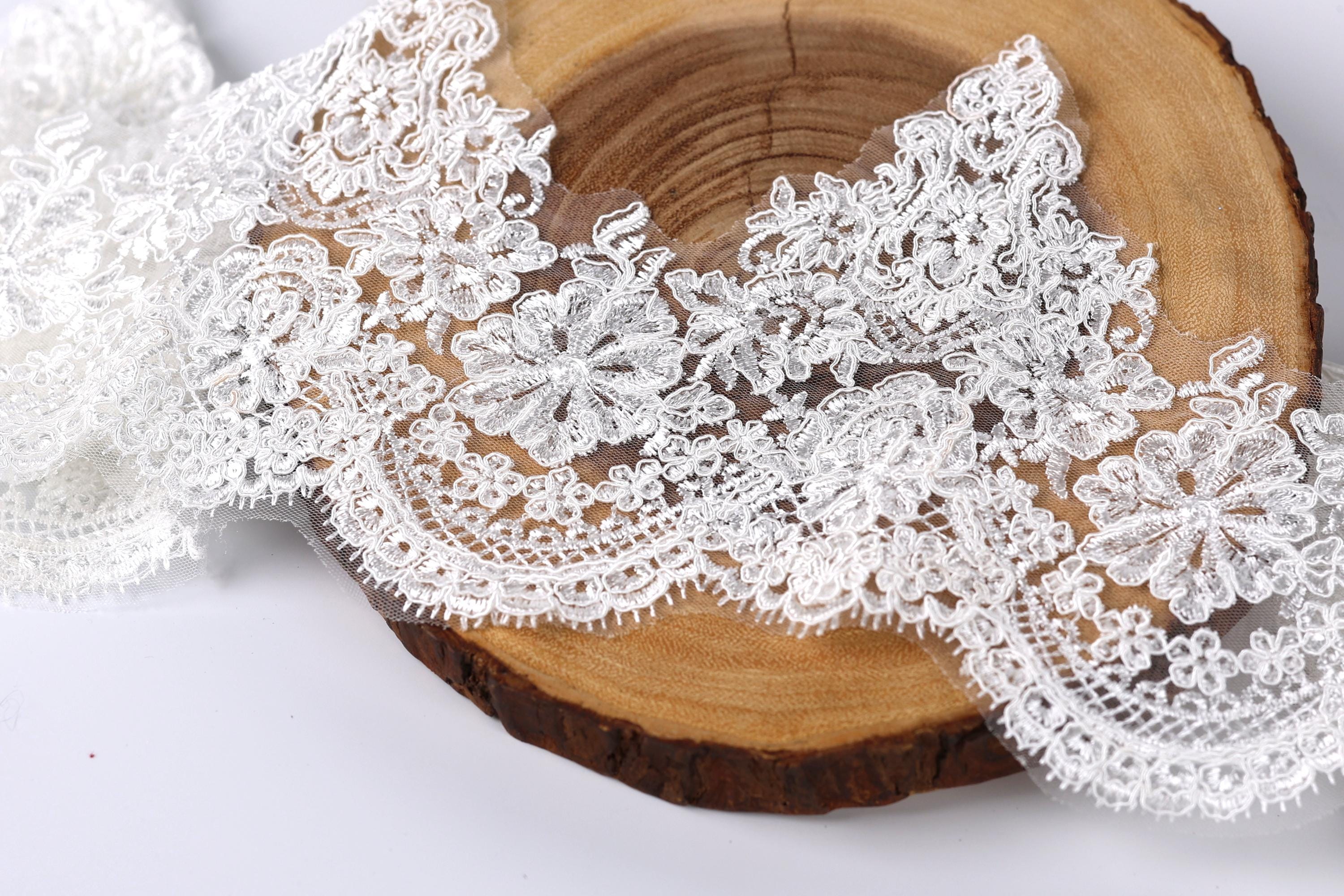 a close-up view of a delicate, intricate lace fabric with a floral pattern. The lace appears to be made of a soft, white material and is displayed on a wooden surface, possibly a piece of driftwood or a wooden board. The lace fabric is spread out, creating a visually appealing and elegant composition.