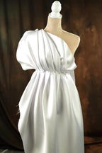 A white dress with a draped, flowing silhouette displayed on a mannequin.