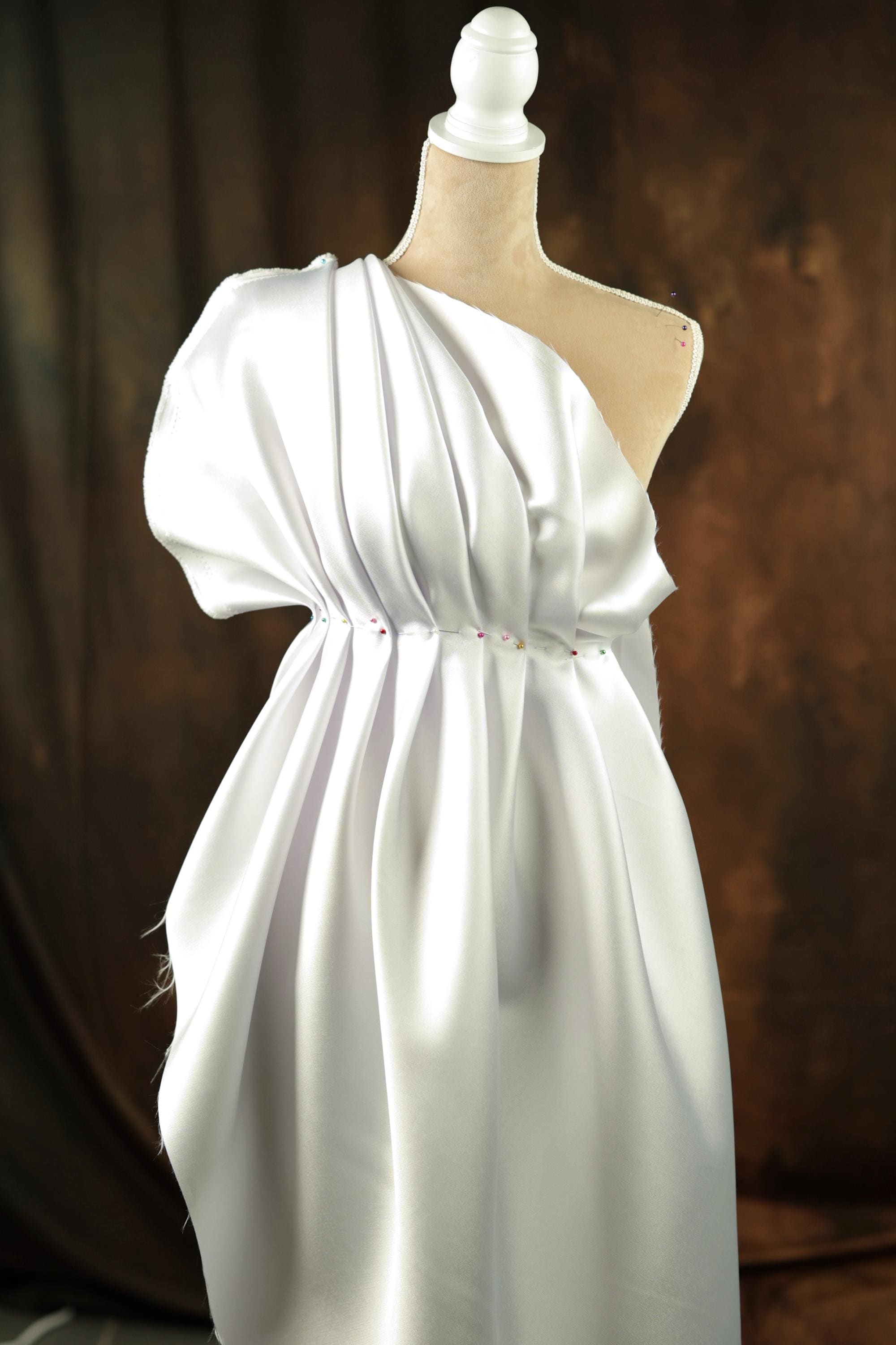 A white dress with a draped, flowing silhouette displayed on a mannequin.