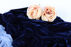 Two light pink roses resting on a crumpled navy blue fabric.