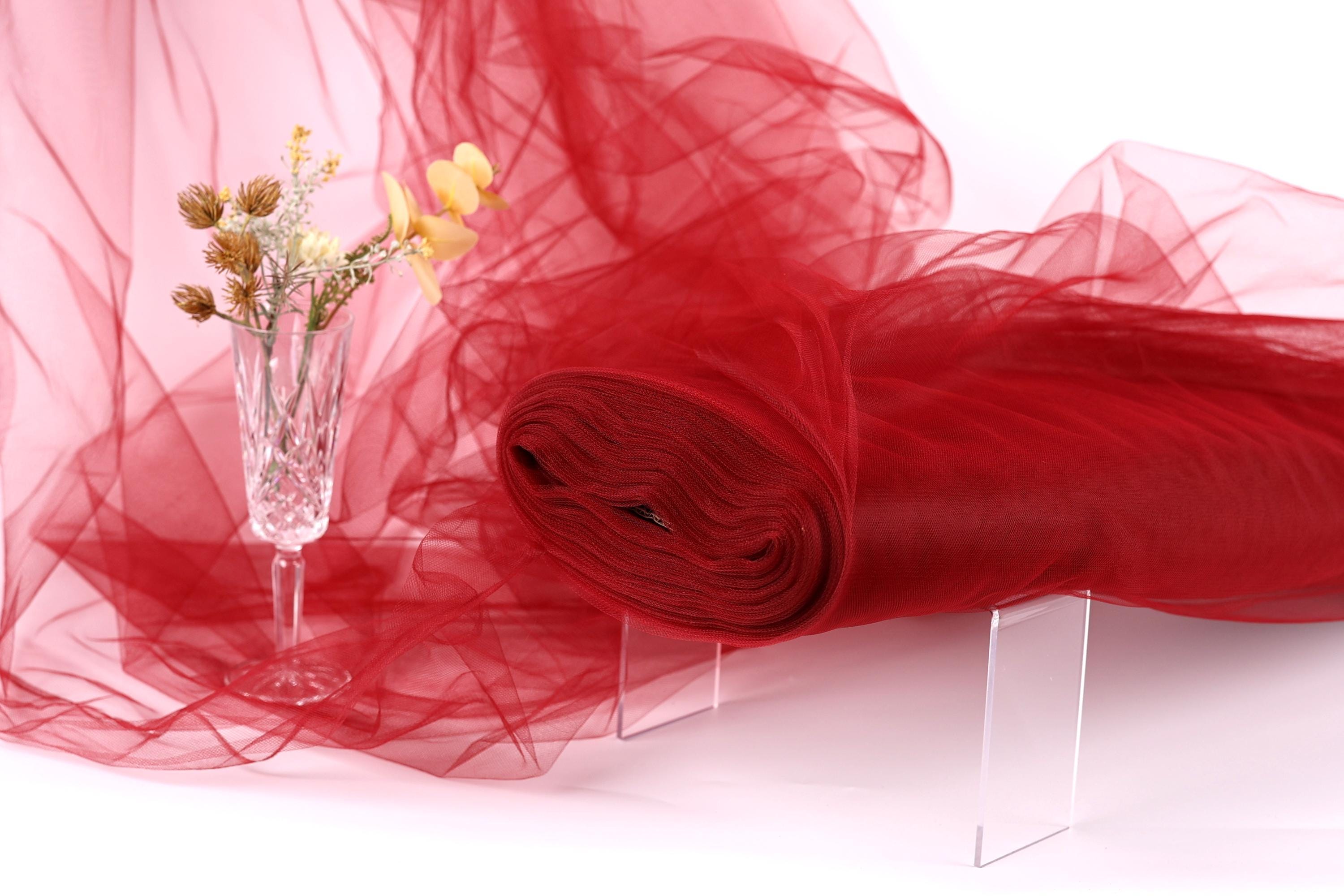 a red fabric roll, a clear glass vase with flowers, and a transparent stand, all set against a pink background.