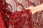 A hand is holding a piece of red sequin fabric with a floral pattern.
