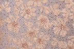 a close-up view of a fabric with a floral pattern, including various shades of pink and beige flowers and leaves. The fabric appears to be embellished with small silver or metallic elements, adding a touch of sparkle to the overall design.