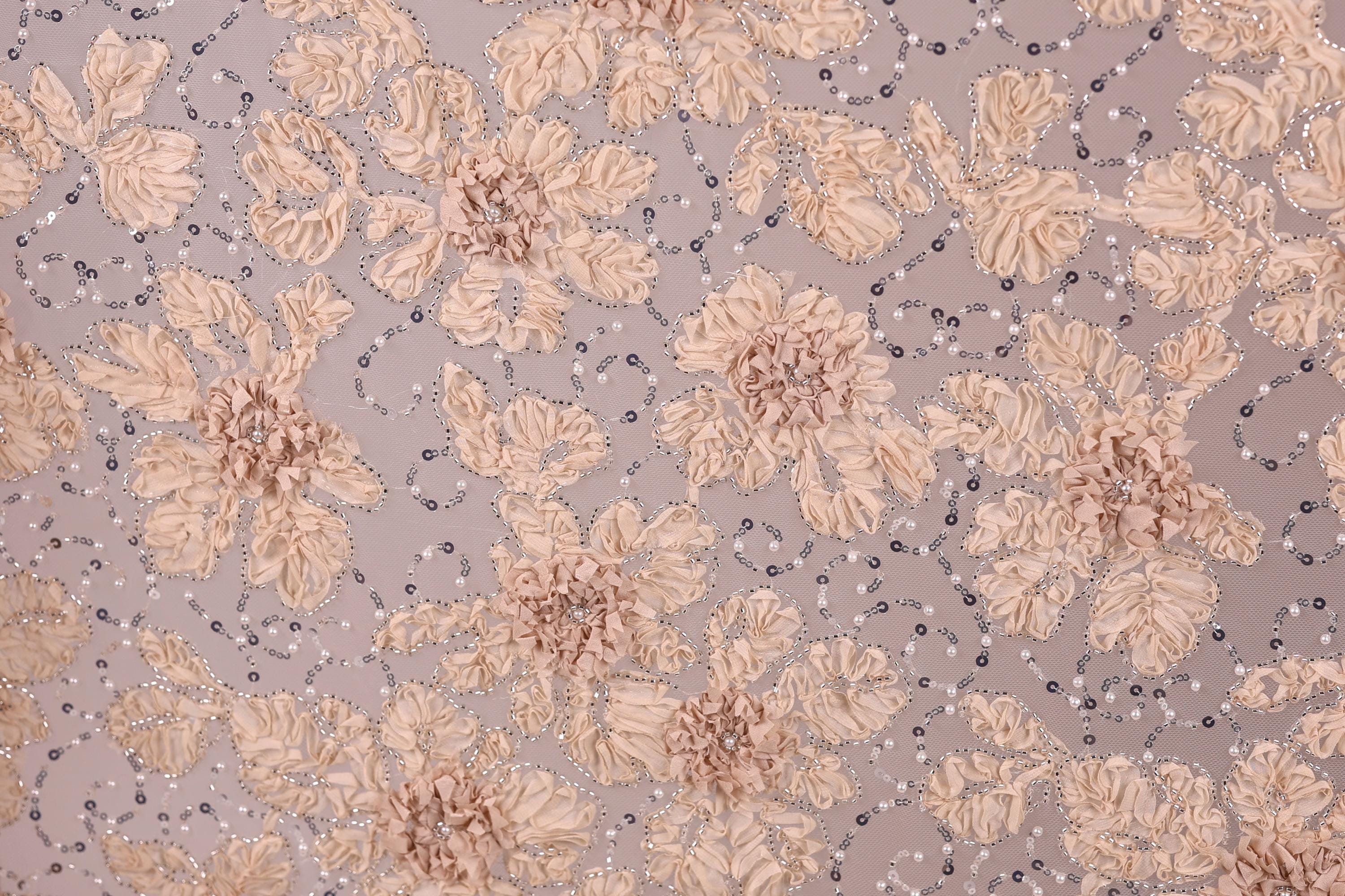a close-up view of a fabric with a floral pattern, including various shades of pink and beige flowers and leaves. The fabric appears to be embellished with small silver or metallic elements, adding a touch of sparkle to the overall design.