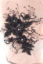 a close-up view of a delicate, intricate black lace piece adorned with small, round beads. The lace is intricately woven with various floral and leaf-like patterns, creating a visually striking and elegant design.