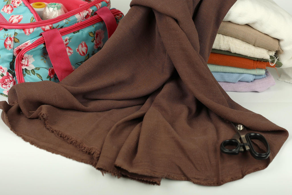 a pile of folded clothes, a pair of scissors, and a floral-patterned bag on a white surface.