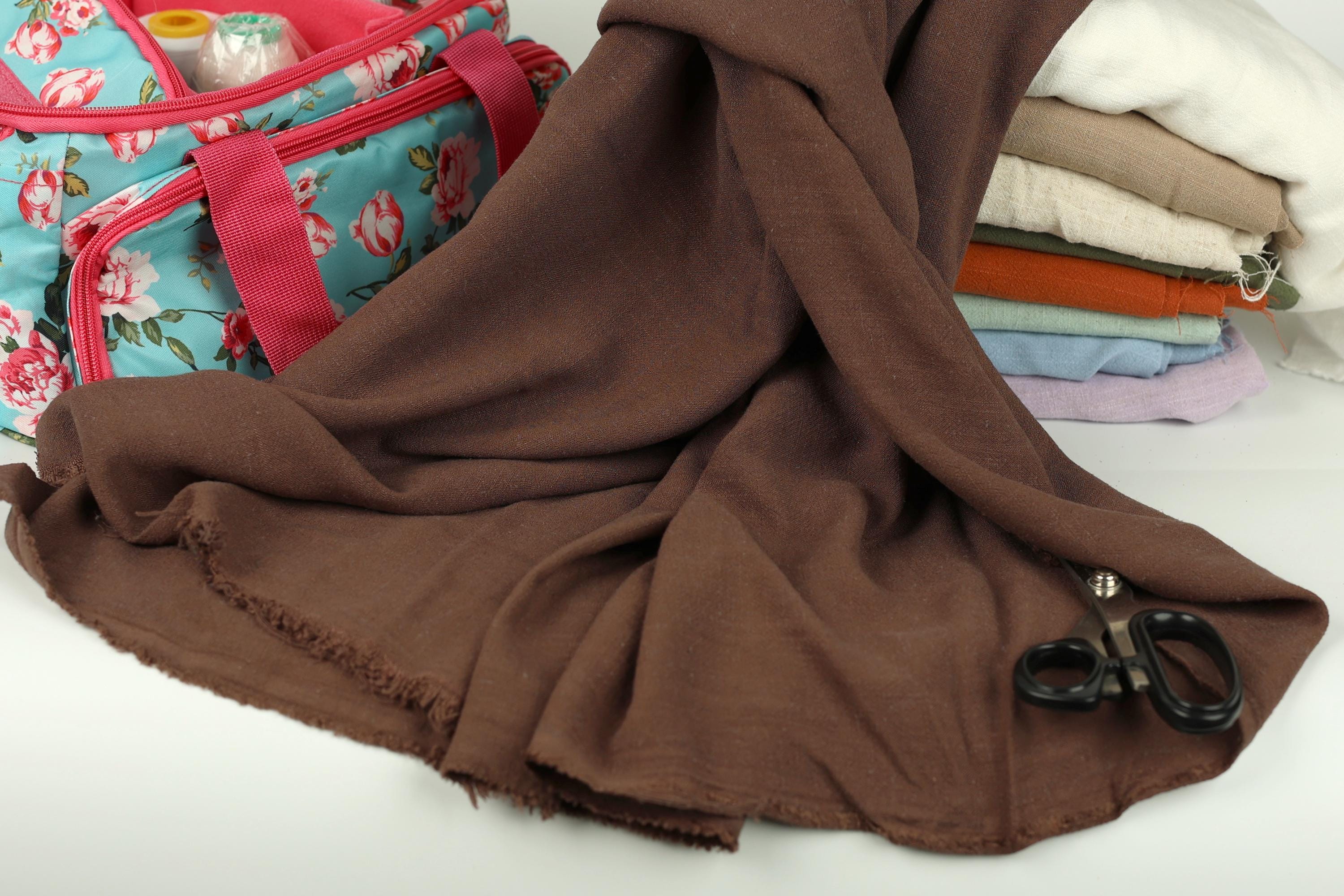 a pile of folded clothes, a pair of scissors, and a floral-patterned bag on a white surface.