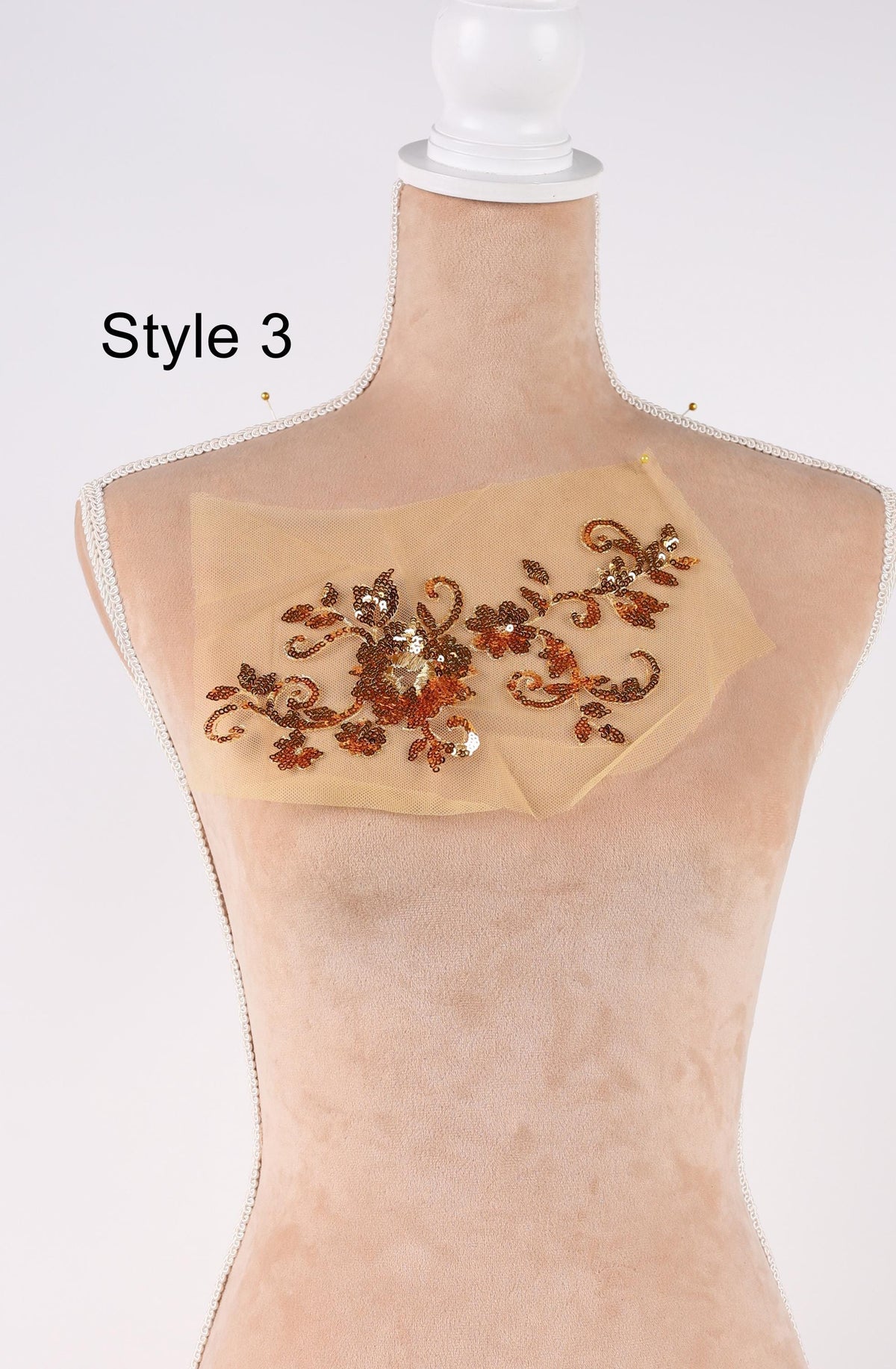 A mannequin with a beige fabric draped over it, featuring a decorative floral pattern in gold and brown colors.