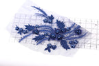 a close-up view of a piece of fabric with a floral design, including blue flowers and leaves. The fabric appears to be a lace or a similar type of material, with a clear ruler visible in the background.