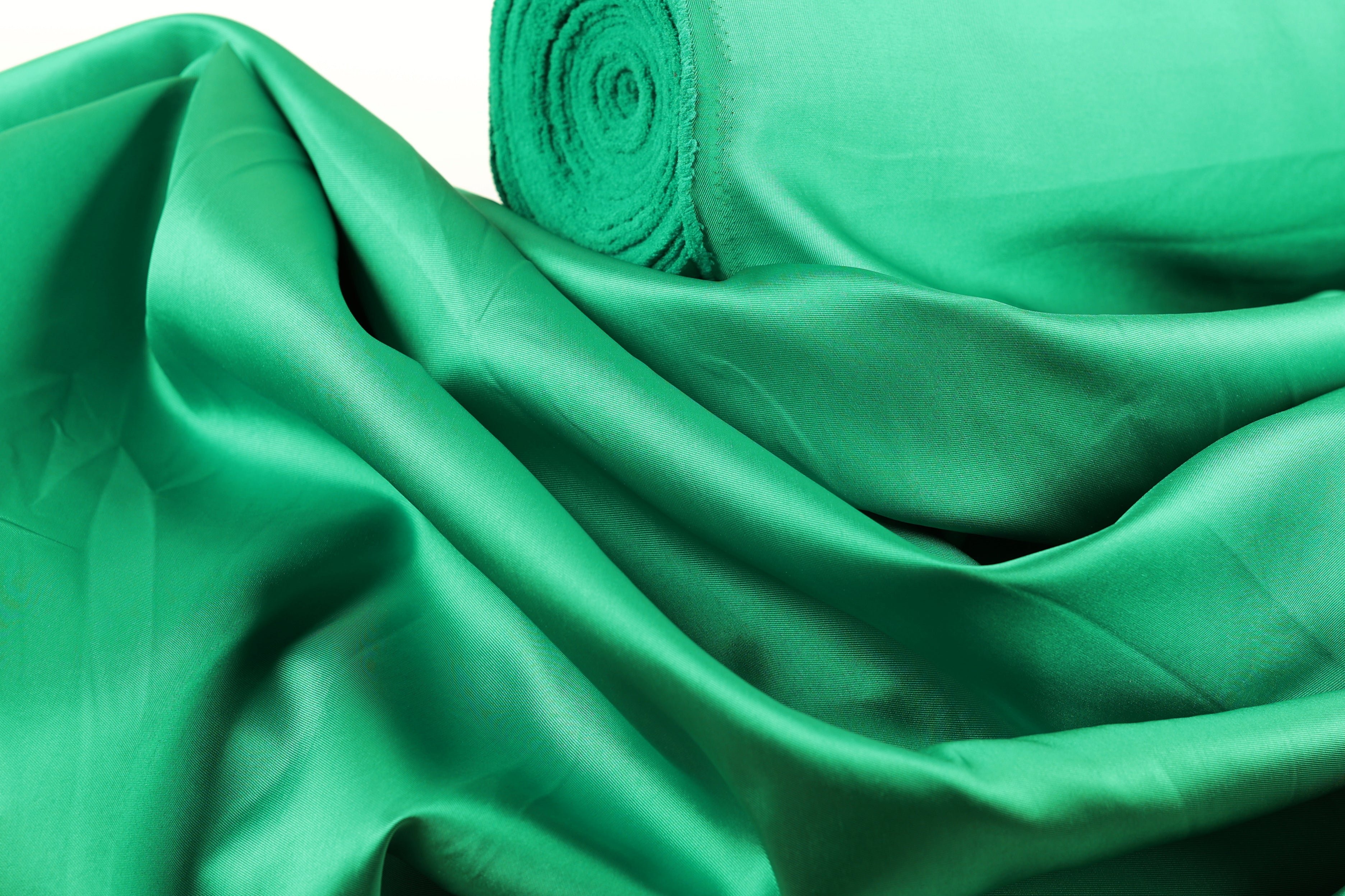 A close-up view of a crumpled, shiny green fabric, possibly silk or satin, with a rolled-up end visible.