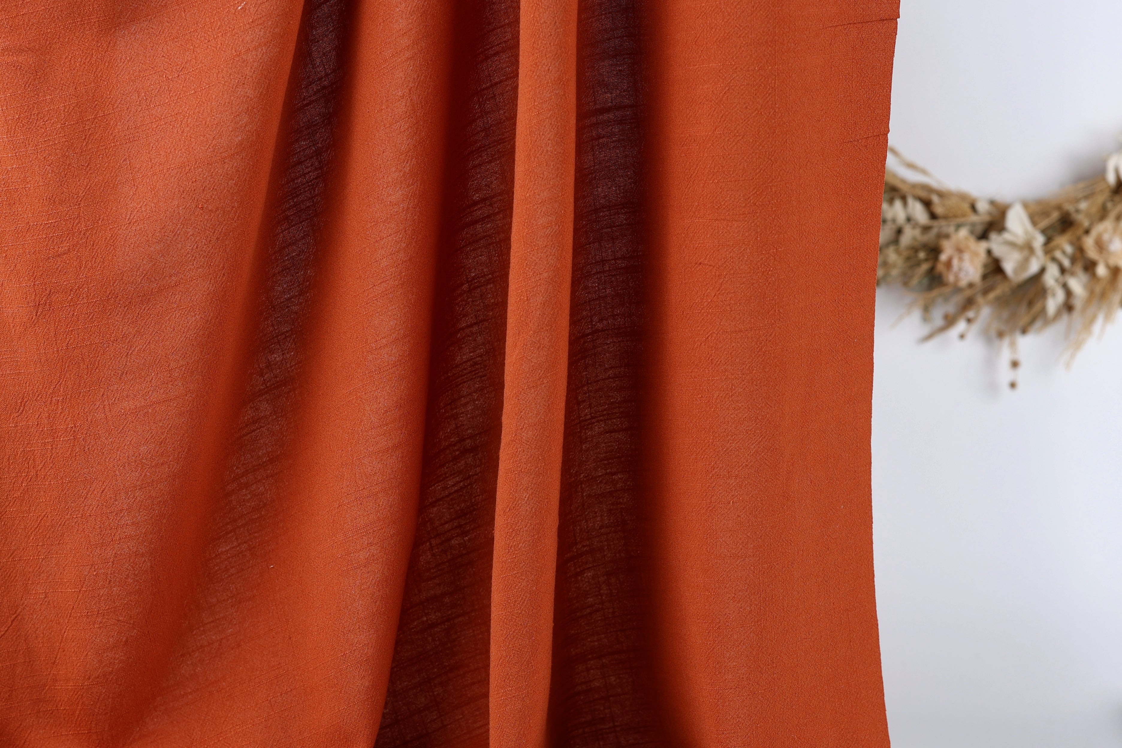 a close-up view of a red fabric, possibly a curtain or a piece of clothing, with a wreath of dried flowers visible in the background.