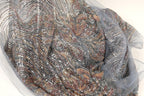 a close-up view of a fabric with a metallic, sequined pattern in shades of gray, silver, and gold. The fabric appears to be a sheer material, with a delicate and intricate design.