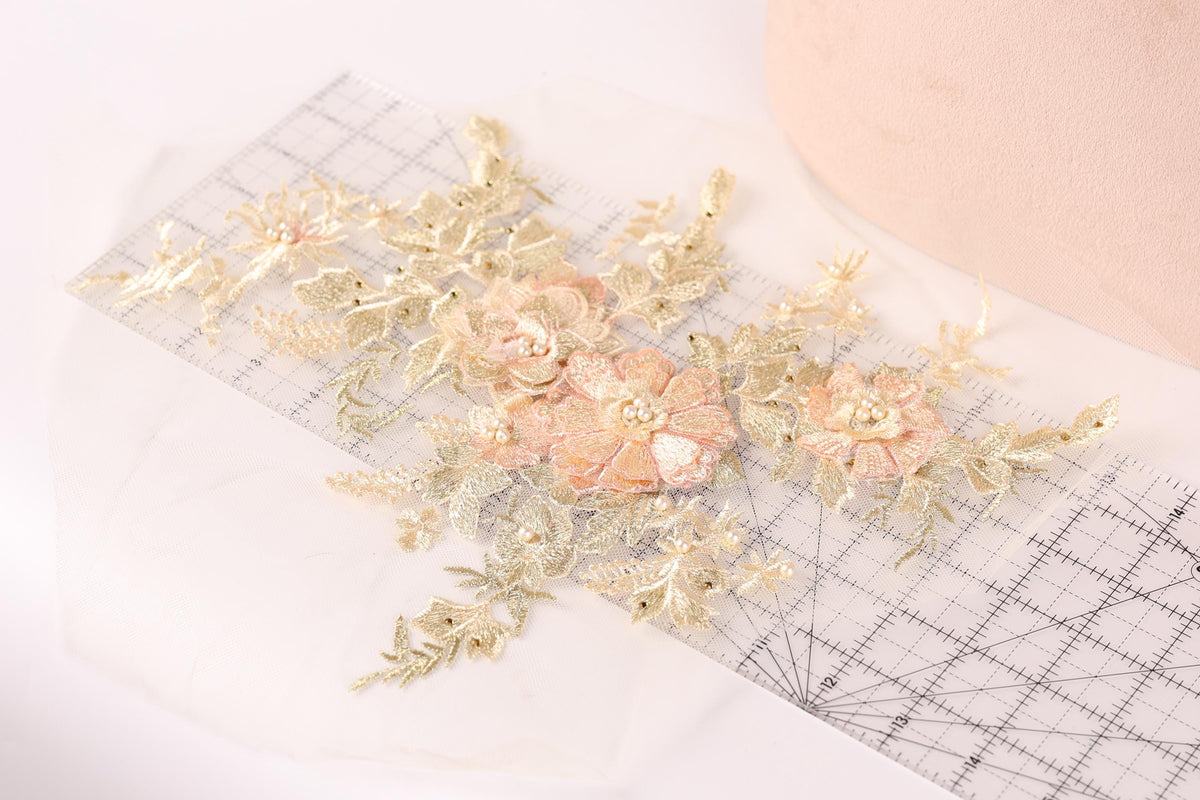 a close-up view of a delicate floral embroidery with gold and white flowers, placed on a transparent surface.