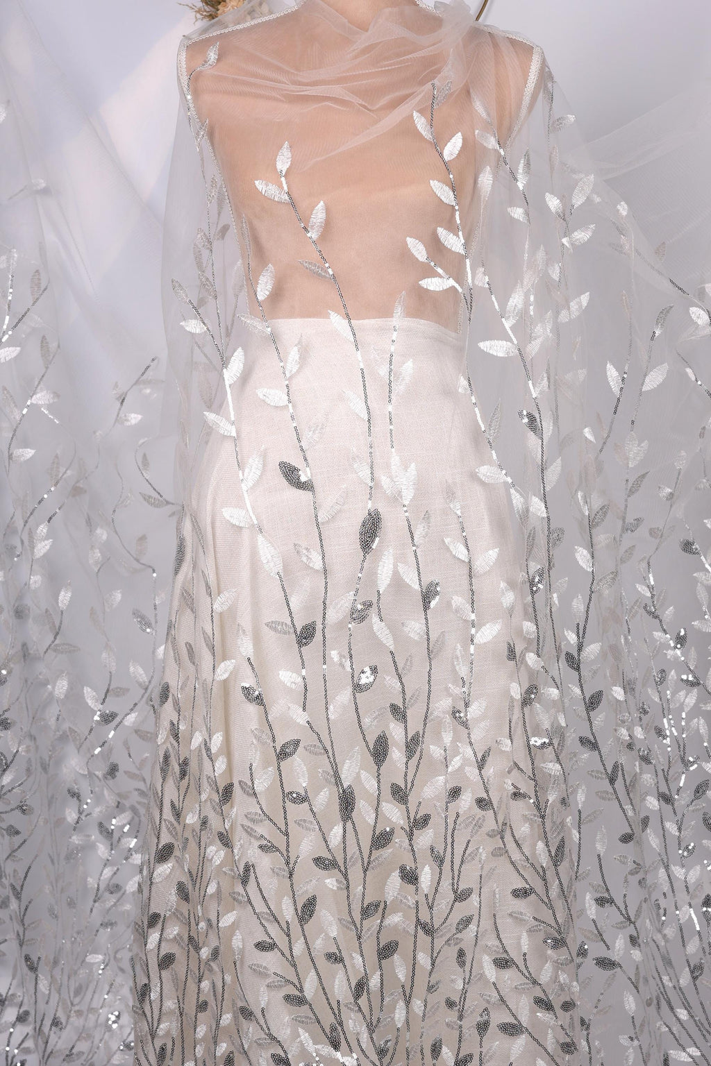 A mannequin wearing a white dress with a sheer, leaf-like pattern on the skirt.