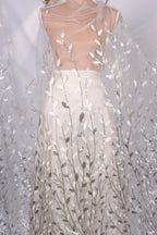 A mannequin wearing a white dress with a sheer, leaf-like pattern on the skirt.