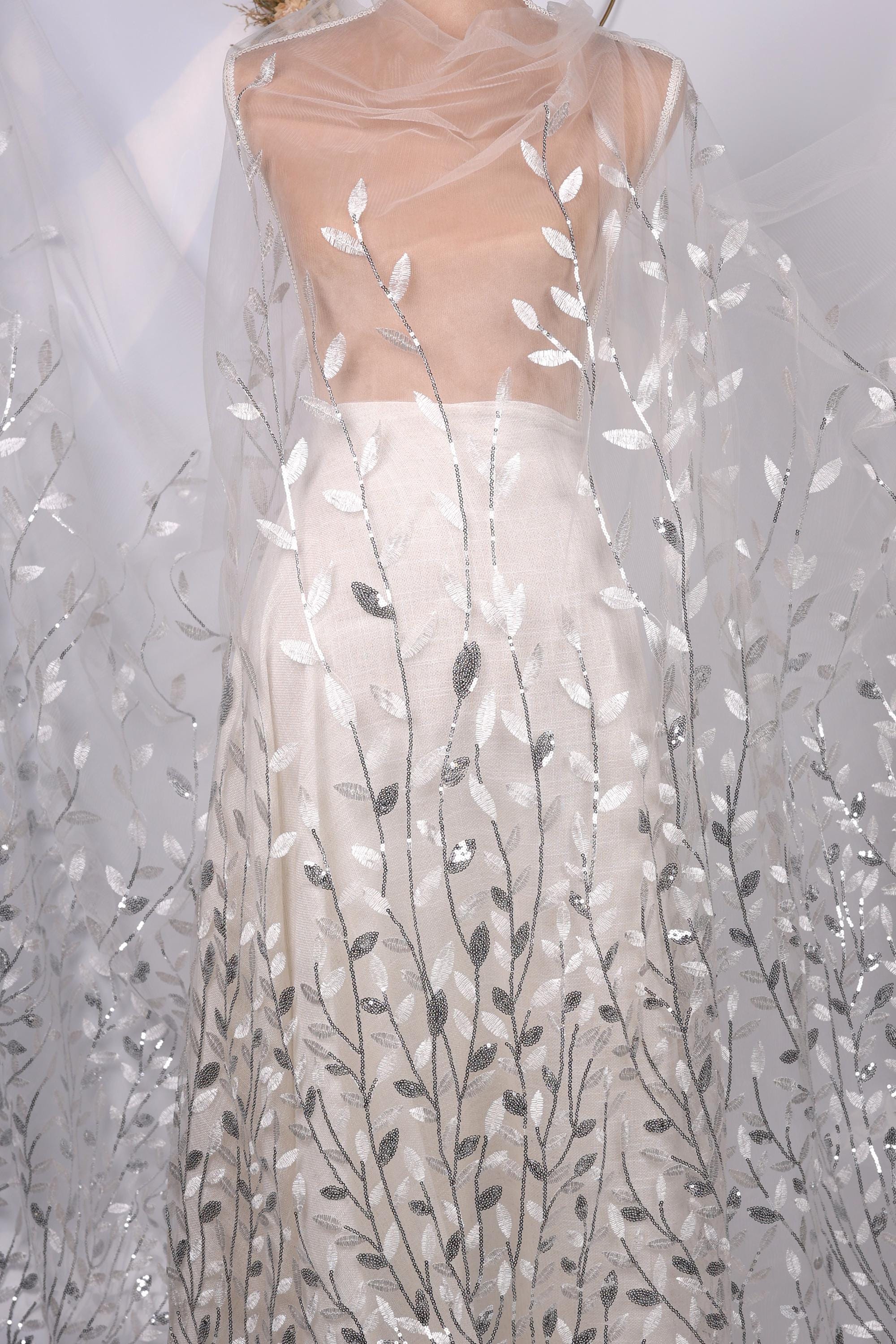 A mannequin wearing a white dress with a sheer, leaf-like pattern on the skirt.