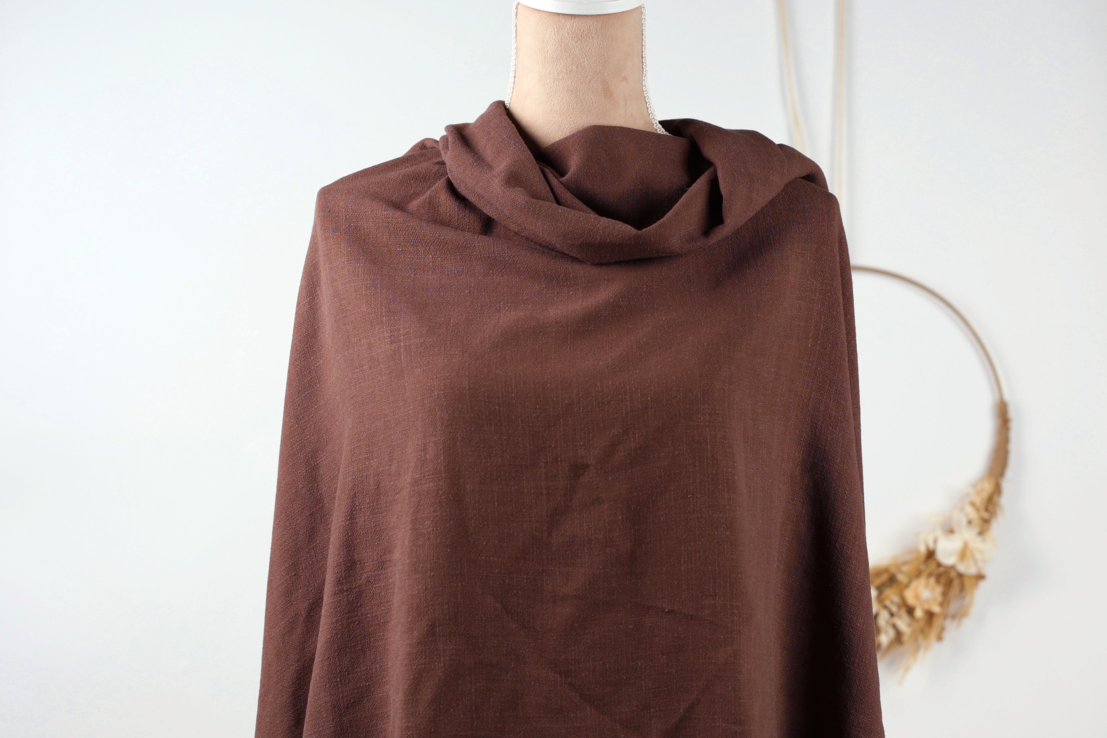 A mannequin wearing a brown, knitted garment with a scarf draped over it, displayed against a white background.