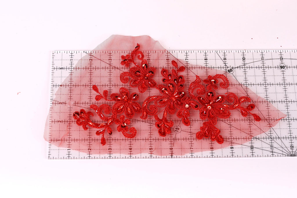 a piece of red fabric with intricate red floral designs, laid out on a transparent ruler for scale.