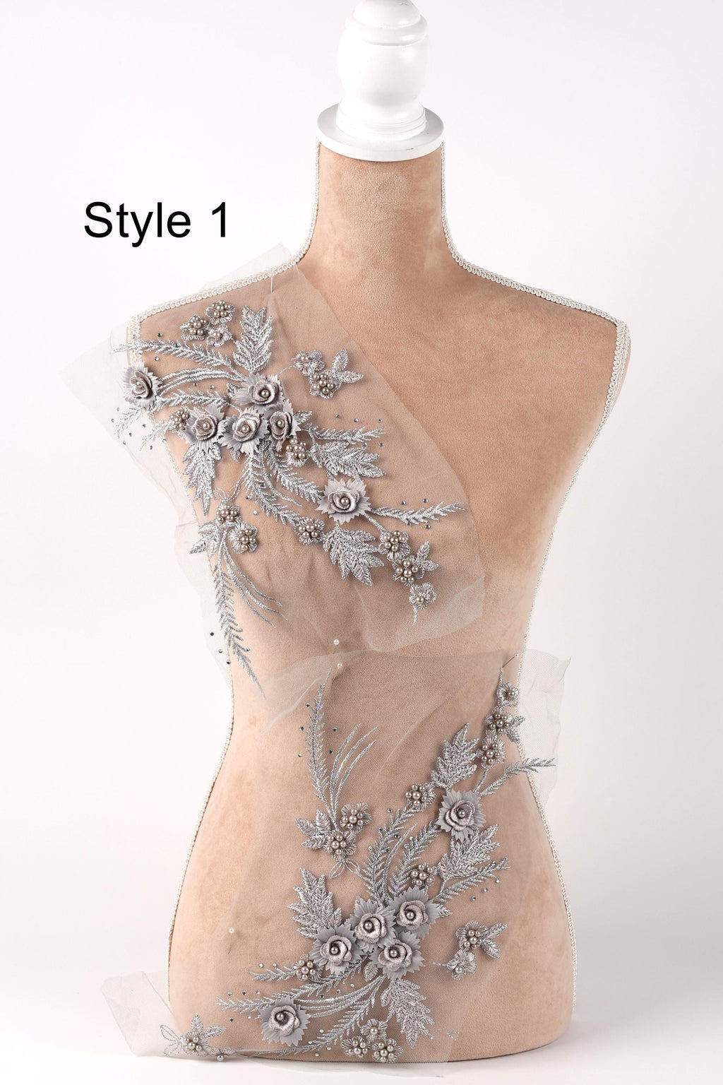 A mannequin with a beige body and a white head, wearing a dress with silver floral embroidery.